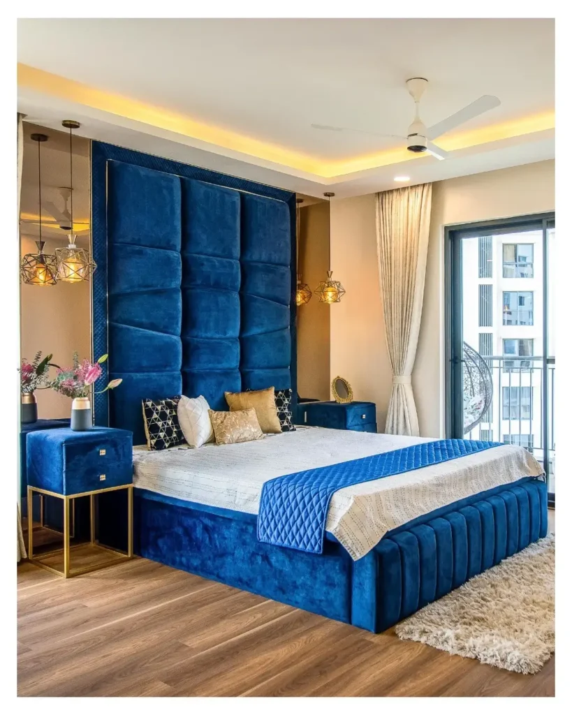 Royal blue velvet upholstered bed with full-height tufted headboard, gold pendant lights, and luxury modern bedroom decor